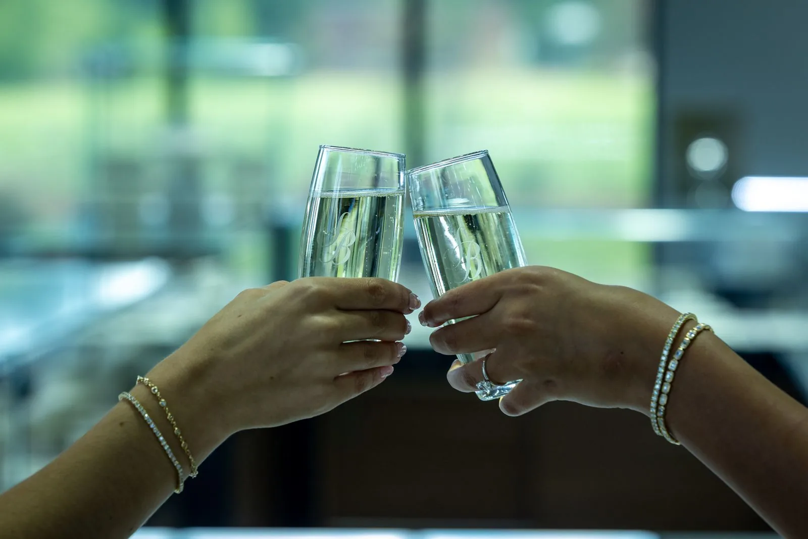 Two people toasting champagne glasses, jewelry visible on the hands