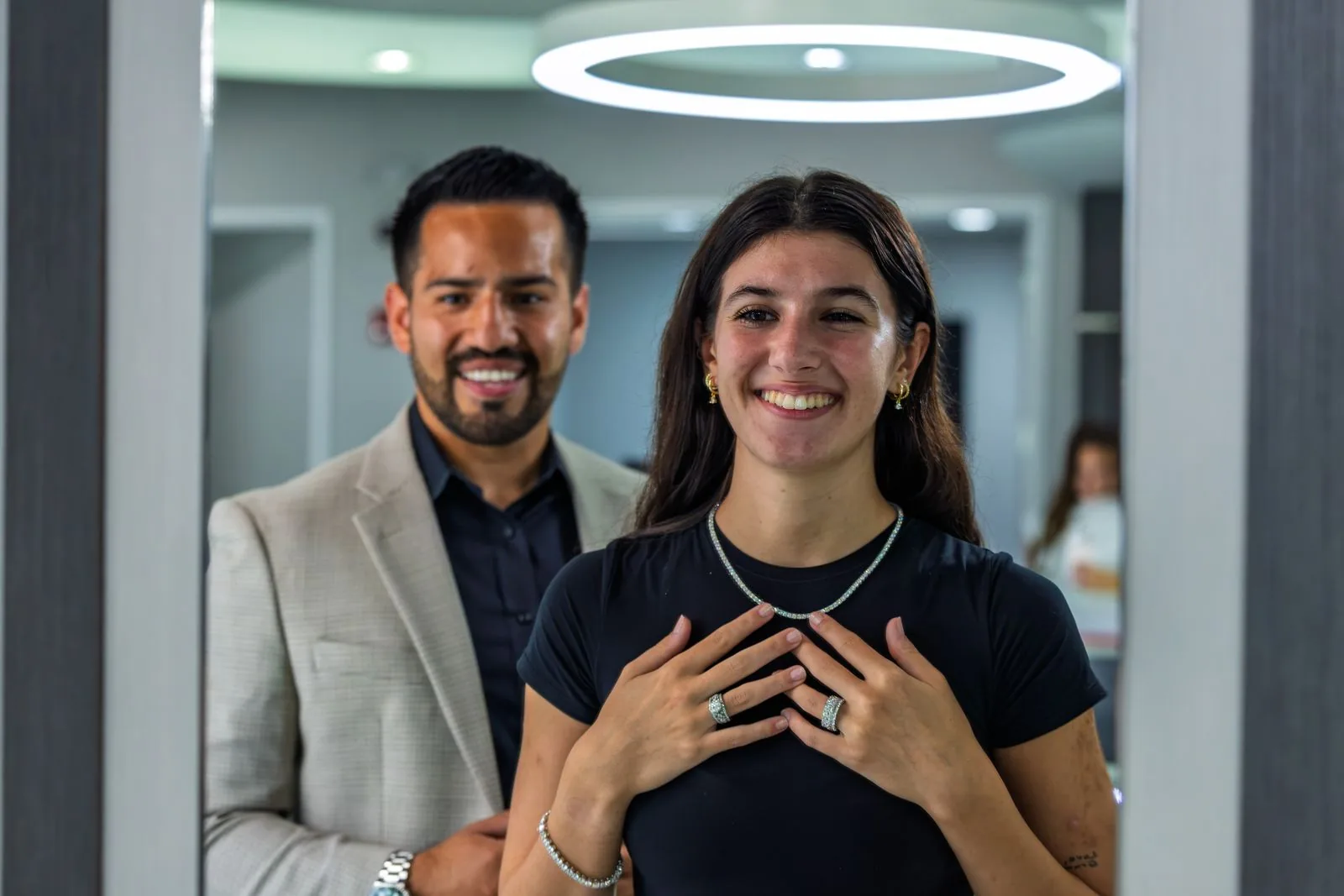 A couple smiling, the woman wearing a necklace, under warm showroom light
